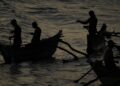Silhouettes of fishermen rowing traditional boats at sunrise in Dickwella, Sri Lanka
