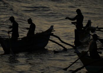 Silhouettes of fishermen rowing traditional boats at sunrise in Dickwella, Sri Lanka