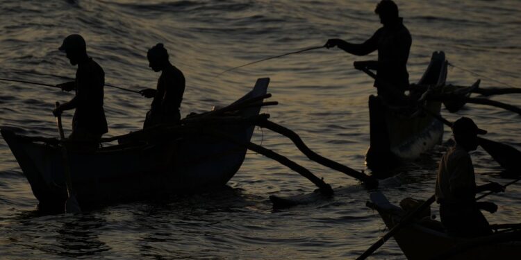 Silhouettes of fishermen rowing traditional boats at sunrise in Dickwella, Sri Lanka