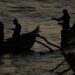 Silhouettes of fishermen rowing traditional boats at sunrise in Dickwella, Sri Lanka